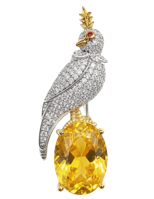 Jewelry item resembling a parrot with a large yellow gemstone on a white background Fleur de Camélia Taya Rhinestone Bird on a Rock Brooch
