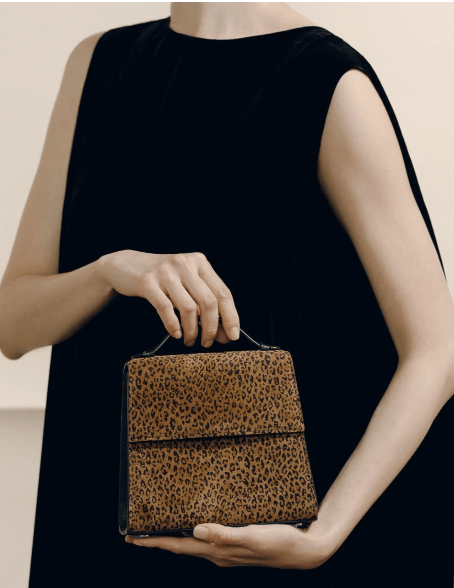Model holding Hunting Season leopard-print suede top handle clutch with black dress