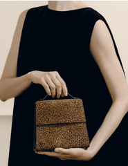 Model holding Hunting Season leopard-print suede top handle clutch with black dress