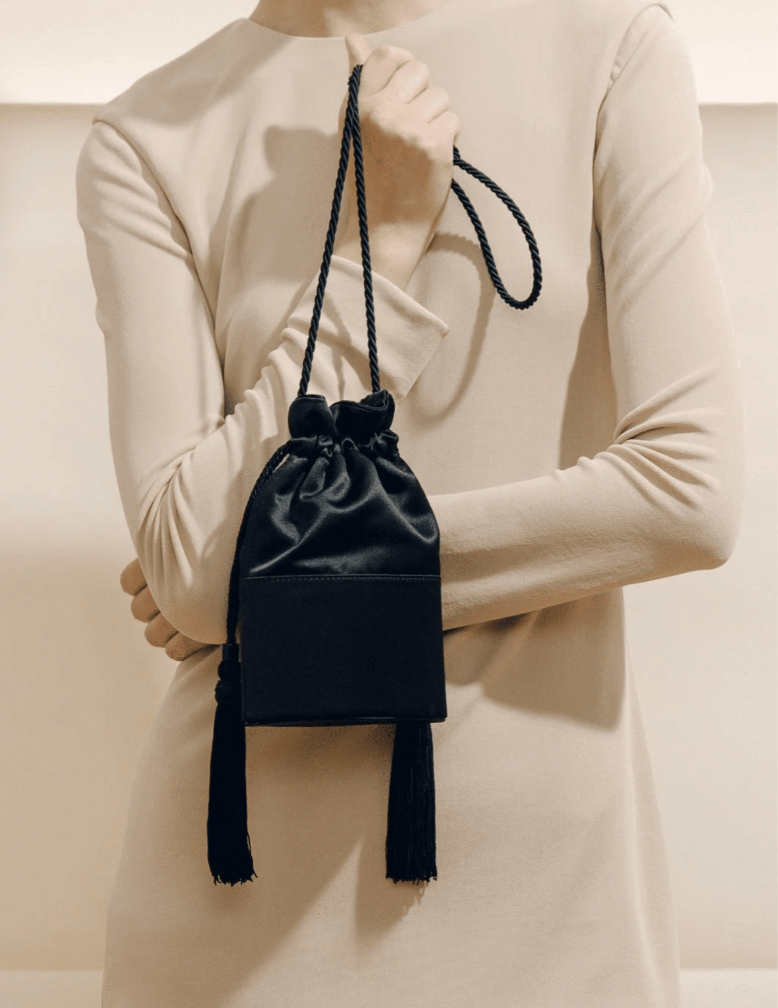 Model holding Hunting Season The Lola black satin bucket bag with cream outfit