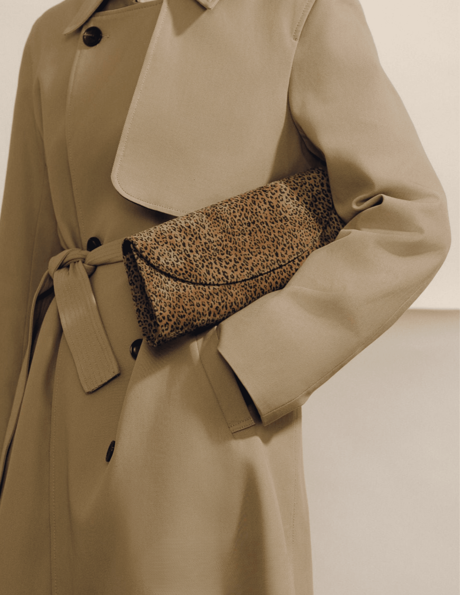 Model holding Hunting Season Opera leopard print suede clutch with beige trench coat
