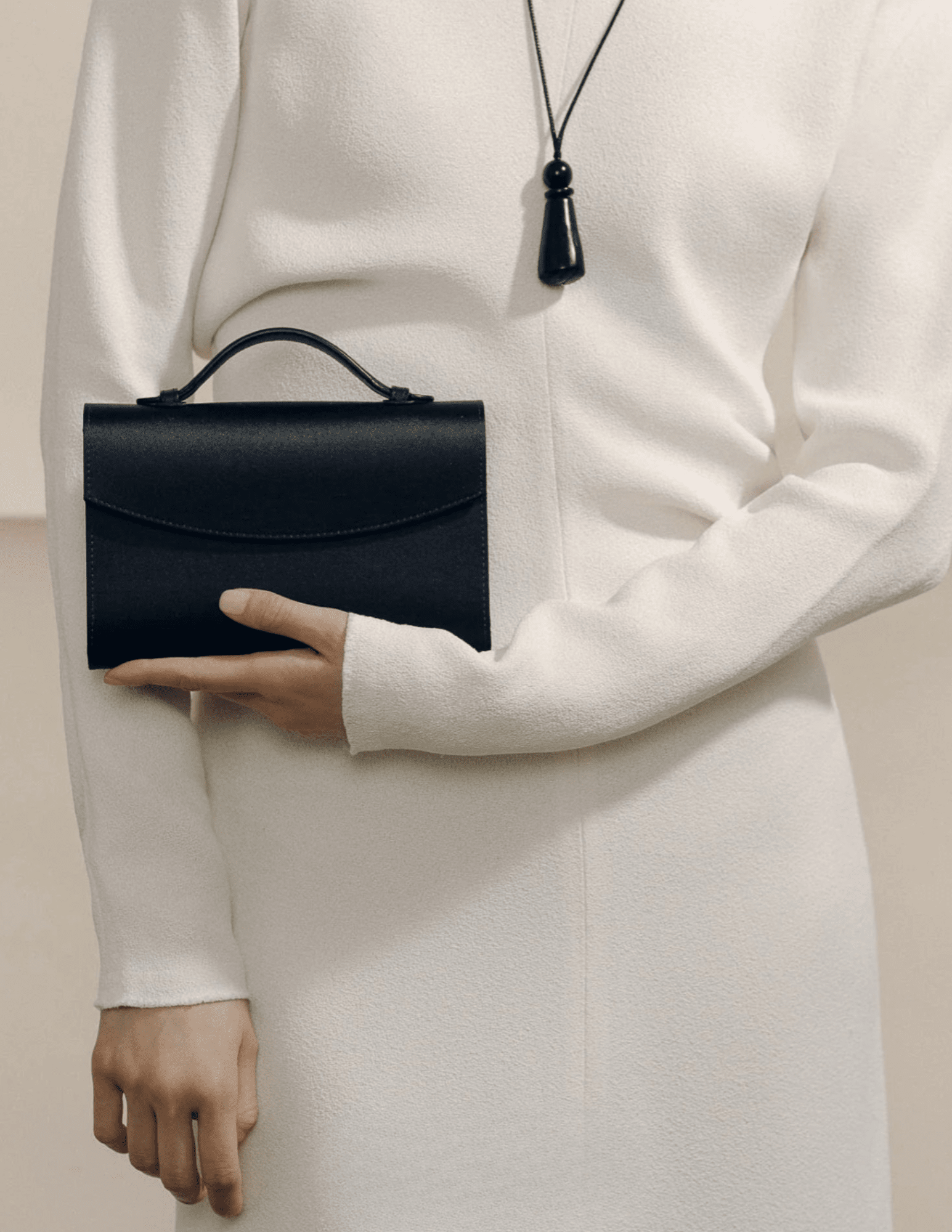 Model holding Hunting Season black satin top handle clutch with elegant cream outfit