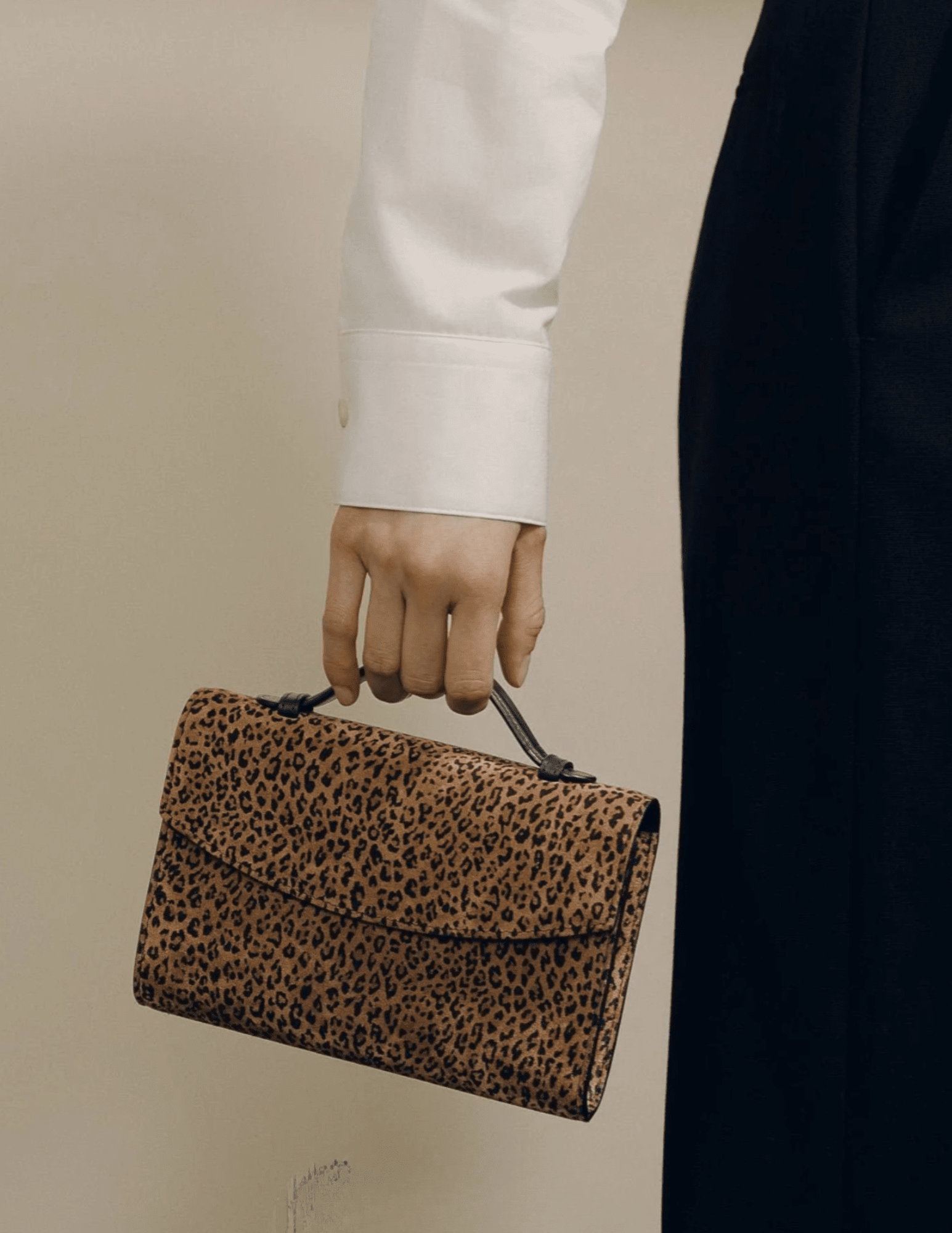 Model carrying Hunting Season leopard print suede clutch by its top handle