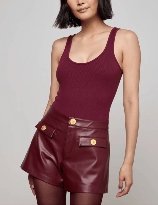 Model wearing L’AGENCE Nica Scoop Neck Bodysuit in Dark Port with burgundy leather shorts, front view.