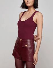 Side view of model wearing L’AGENCE Nica Scoop Neck Bodysuit in Dark Port with leather shorts.