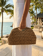 Model holding St. Barths natural straw pouch clutch at a resort